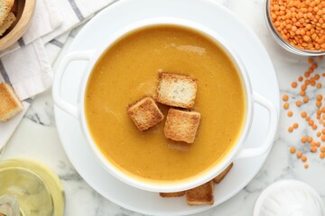 Delicious lentil cream soup served with croutons on white marble table, flat lay