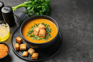 Delicious lentil cream soup served with croutons on grey table, closeup. Space for text
