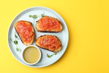Tasty bread with tomato, microgreens and oil on yellow background, top view. Space for text