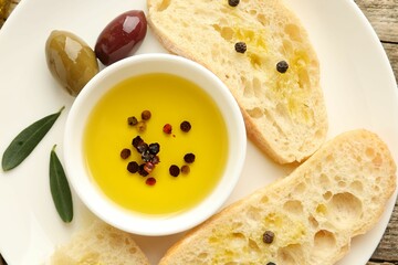 Slices of bread with oil, spices and olives on wooden table, top view