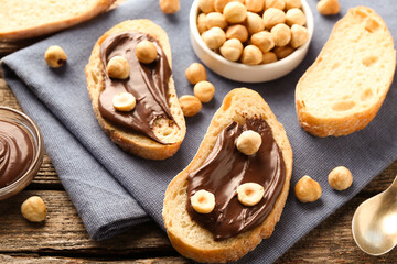 Slices of bread with chocolate spread and hazelnuts on wooden table