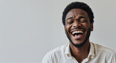 Obraz premium black African 20s man on white plain bright background happy laughing hysterical looking at camera portrait banner with copy space ad concept marketing