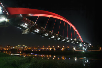 The Rainbow Bridge becomes a radiant passage through the night, reflecting vibrant lights on the calm Keelung River below.
