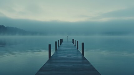 Obraz premium Misty lake with wooden dock extending to fog.