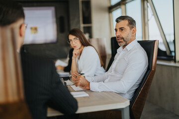 A multicultural group of business people participating in a serious discussion around a conference table, focusing on strategic planning and collaboration in a modern office setting.
