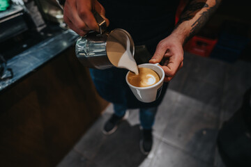 A barista is skillfully making a latte by pouring warm milk into espresso, showcasing craftsmanship.