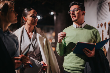 People in a museum setting discuss in an informative and engaging environment, focusing on posters and exhibits on the wall, conveying learning, education, and collaboration in a cultural space.