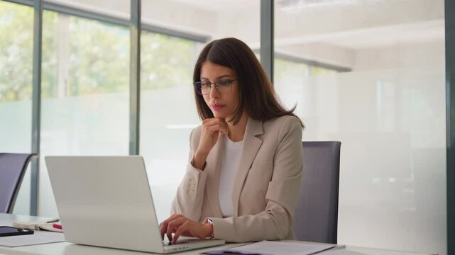 Young 30s it specialist latin hispanic business lady working on laptop pc sitting at desk in modern office space. Middle eastern woman using computer technology app for work online, smiling happy