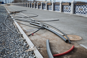 A messy and tangled mass of various wires is carelessly spread out on the ground near a bridge,...
