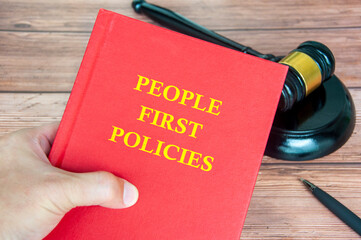 Hand holding People First Policies book with gavel on a wooden table background