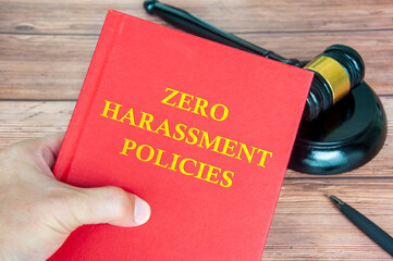 Hand holding Zero Harassment Policies book with gavel background. Harassment free concept