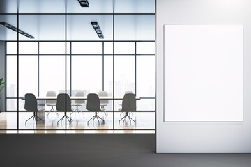 Modern office interior with empty vertical poster frame on wall near glass-walled conference room overlooking cityscape in daylight. 3D Rendering