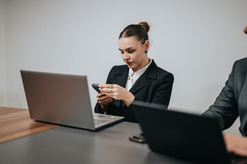 Business professional seated at a desk interacting with a smart phone during a corporate setting. Office environment highlights collaboration, technology use, and productivity. The atmosphere suggests