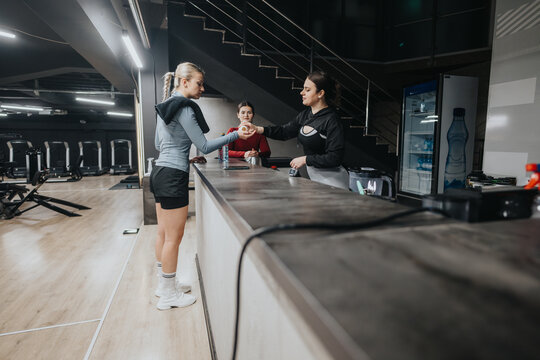 Three women at a gym reception desk engaging in a friendly conversation within the modern fitness environment.