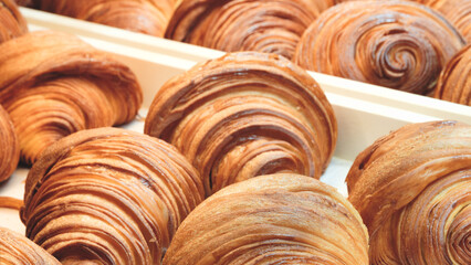 A row of croissants are displayed in a bakery. croissants are golden brown and have a flaky, buttery texture. display is arranged in a way that highlights the variety of shapes