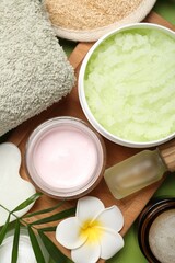 Different body care products, plumeria flowers and twig on green background, flat lay