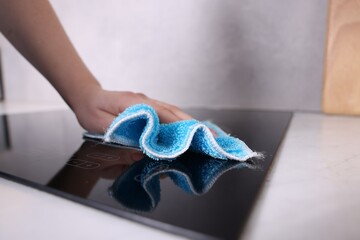 Woman cleaning induction cooktop with rag indoors, closeup