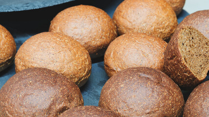 A row of brown and white bread rolls on a black plate. The brown rolls are slightly larger than the white ones