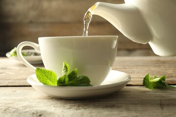 Pouring freshly brewed tea from teapot into cup at wooden table, closeup