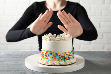 Woman refusing to eat cake at grey wooden table, selective focus. Food allergy concept