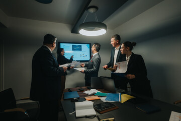 A group of business professionals discusses graphs and charts displayed on a presentation screen during a collaborative meeting in a modern conference room.