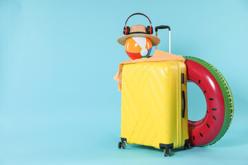 Bright inflatable ring, other different accessories, headphones and suitcase on light blue background, space for text