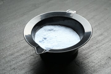 Bowl with hair bleaching powder on black table, closeup
