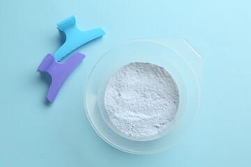 Bleaching powder and hairdresser's tools on light blue background, flat lay