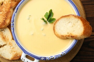 Tasty cheese dipping sauce in bowl and croutons on wooden table, top view