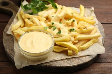 Delicious cheese sauce in bowl, French fries and parsley on wooden table, closeup