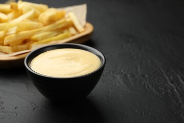 Tasty cheese sauce in bowl and French fries on black table, closeup. Space for text