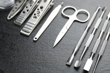 Set of different manicure tools on black textured table, closeup. Space for text