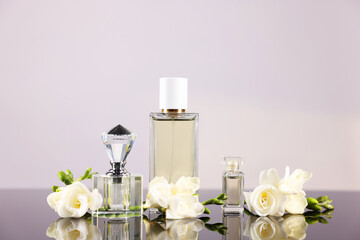 Bottles of aromatic perfume and flowers on mirror surface against light grey background