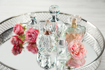 Bottles of perfume and beautiful flowers on tray, closeup