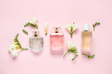 Bottles of perfume and beautiful flowers on pink background, flat lay