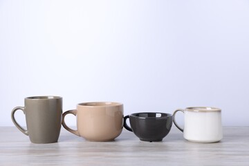 Many colorful cups on light wooden table against white background. Space for text