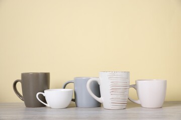 Many colorful cups on light wooden table against beige background. Space for text