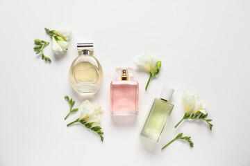 Flat lay composition with bottles of aromatic perfume and beautiful flowers on white background