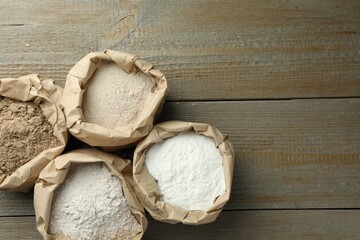 Different types of flour in paper bags on wooden table, flat lay. Space for text