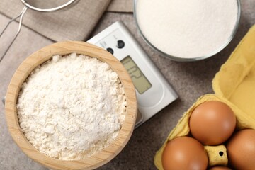 Digital kitchen scale with bowl of flour and other products on grey textured table, flat lay