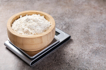 Digital kitchen scale with bowl of flour on grey textured table, closeup