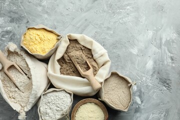 Different types of flour in bags on grey textured table, flat lay. Space for text