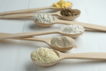 Different types of flour in spoons on white wooden table, closeup
