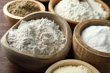 Different types of flour in bowls on wooden table, closeup