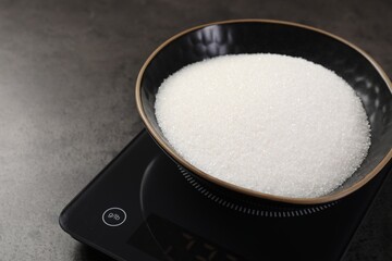 Digital kitchen scale with bowl of sugar on grey table, closeup