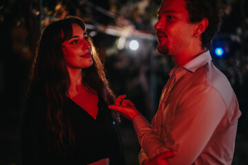 Two individuals engaged in a lively discussion, featured under decorative festive lighting,...