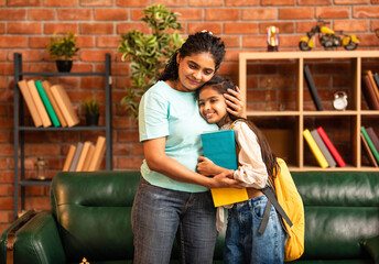 Caring Indian Asian mother packing daughter's school bag with books and lunch, hugging her goodbye