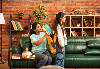 Caring Indian Asian mother packing daughter's school bag with books and lunch, hugging her goodbye
