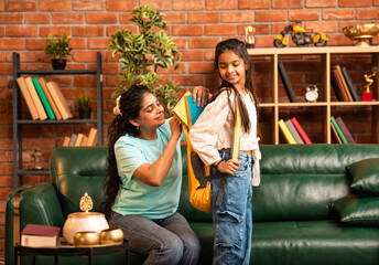 Caring Indian Asian mother packing daughter's school bag with books and lunch, hugging her goodbye
