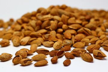 Raw almonds with shells scattered on a white surface, showcasing their natural texture